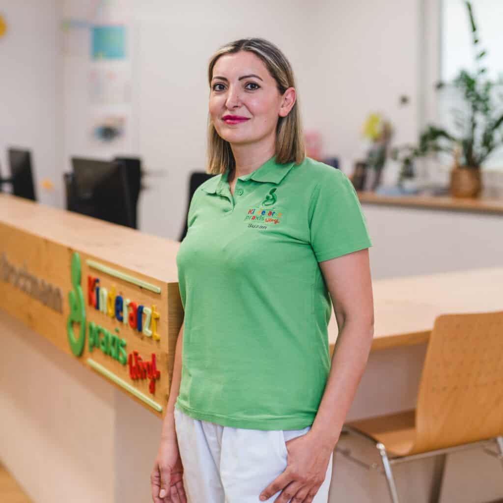 Suzan ist Mitarbeiterin in der Praxis und steht vor dem Tresen. Sie trägt ein grünes Shirt.